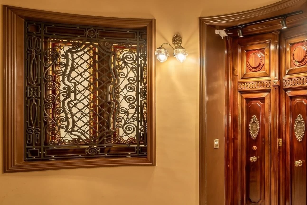 Rellano de la planta primera con vidriera emplomada tras una reja de forja modernista y puerta de madera noble